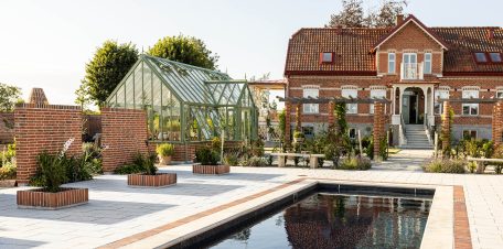 Exklusivt växthus i mossgrön aluminium från Vansta Trädgård, placerat i en nyanlagd trädgård vid ett restaurerat tegelhus i Löderup på Österlen.