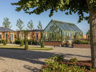Exklusivt växthus i mossgrön aluminium från Vansta Trädgård, placerat i en nyanlagd trädgård vid ett restaurerat tegelhus i Löderup på Österlen.