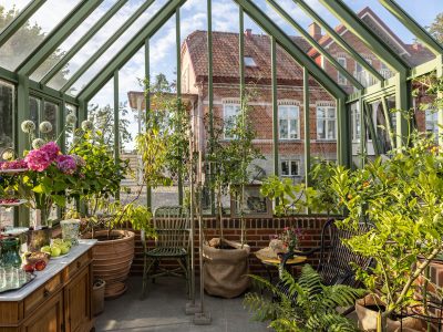 Exklusivt växthus i mossgrön aluminium från Vansta Trädgård, placerat i en nyanlagd trädgård vid ett restaurerat tegelhus i Löderup på Österlen.