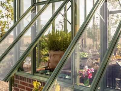 Exklusivt växthus i mossgrön aluminium från Vansta Trädgård, placerat i en nyanlagd trädgård vid ett restaurerat tegelhus i Löderup på Österlen.