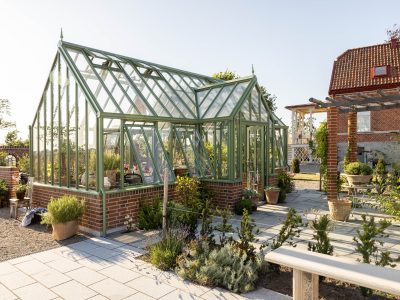 Exklusivt växthus i mossgrön aluminium från Vansta Trädgård, placerat i en nyanlagd trädgård vid ett restaurerat tegelhus i Löderup på Österlen.