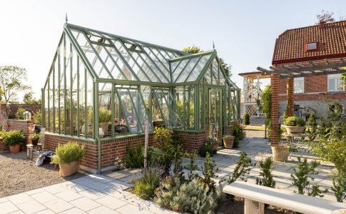 Exklusivt växthus i mossgrön aluminium från Vansta Trädgård, placerat i en nyanlagd trädgård vid ett restaurerat tegelhus i Löderup på Österlen.